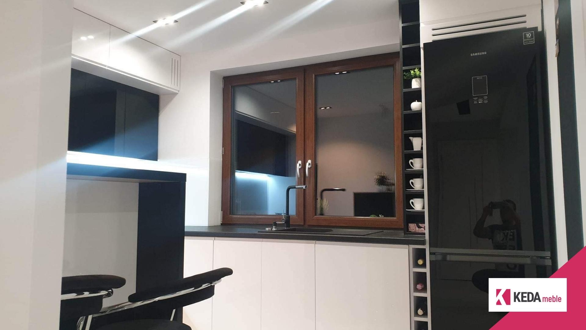 Kuchnia jest sercem domu, miejscem, gdzie rodzinne tradycje łączą się z nowoczesnym designem. W naszej ofercie znajdziesz rozwiązania, które harmonijnie łączą elegancję z funkcjonalnością, tworząc przestrzeń idealną dla każdej rodziny. Szczególnie polecamy biało-czarne kuchnie, które stanowią szczyt elegancji i są praktycznym wyborem dla każdego, kto ceni sobie styl i funkcjonalność w jednym. Elegancja w Kolorach: Biało-Czarne Kuchnie Kombinacja bieli i czerni w kuchni to ponadczasowy wybór, który nigdy nie wychodzi z mody. Białe powierzchnie odbijają światło, sprawiając, że kuchnia wydaje się większa i jaśniejsza. Czarne akcenty dodają z kolei głębi i charakteru, tworząc wyrafinowany kontrast. Duża Przestrzeń Robocza – Klucz do Funkcjonalności Przestronny blat roboczy to podstawa każdej dobrze zaprojektowanej kuchni. Pozwala na swobodną pracę i przygotowywanie posiłków bez zbędnego chaosu. W naszych projektach kładziemy duży nacisk na ergonomiczne rozmieszczenie elementów, aby każda czynność kuchenna była przyjemnością. Listwa LED – Rewolucja w Oświetleniu Kuchennym Odpowiednie oświetlenie to kluczowy element każdej kuchni. Nasze listwy LED nie tylko efektownie prezentują się w przestrzeni, ale także zapewniają doskonałe oświetlenie robocze, które jest niezbędne podczas przygotowywania posiłków. To praktyczne i energooszczędne rozwiązanie, które dodatkowo podkreśla nowoczesny charakter kuchni. Otwarte Półki – Praktyczne i Dekoracyjne Rozwiązanie Otwarte półki w słupku kuchennym to idealne miejsce na przechowywanie butelek wina, oliwy, czy ulubionych kubków do kawy. Dzięki temu Twoje ulubione przedmioty będą zawsze pod ręką, a jednocześnie staną się częścią dekoracji kuchni. Kuchnie na Wymiar – Twój Indywidualny Projekt Dołącz do grona zadowolonych klientów, zamawiając kuchnię na wymiar. Nasze projekty są w pełni dostosowane do potrzeb i oczekiwań każdego klienta. Tworzymy kuchnie, które są nie tylko piękne, ale przede wszystkim praktyczne i funkcjonalne. Podsumowanie Nasze biało-czarne kuchnie to idealne połączenie elegancji i funkcjonalności. Jeśli marzysz o kuchni, która będzie nie tylko piękna, ale także praktyczna i wygodna, zapraszamy do kontaktu. Zrealizujemy dla Ciebie projekt, który spełni wszystkie Twoje oczekiwania.