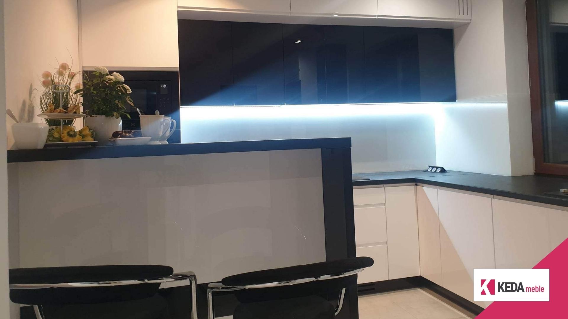 Kuchnia jest sercem domu, miejscem, gdzie rodzinne tradycje łączą się z nowoczesnym designem. W naszej ofercie znajdziesz rozwiązania, które harmonijnie łączą elegancję z funkcjonalnością, tworząc przestrzeń idealną dla każdej rodziny. Szczególnie polecamy biało-czarne kuchnie, które stanowią szczyt elegancji i są praktycznym wyborem dla każdego, kto ceni sobie styl i funkcjonalność w jednym. Elegancja w Kolorach: Biało-Czarne Kuchnie Kombinacja bieli i czerni w kuchni to ponadczasowy wybór, który nigdy nie wychodzi z mody. Białe powierzchnie odbijają światło, sprawiając, że kuchnia wydaje się większa i jaśniejsza. Czarne akcenty dodają z kolei głębi i charakteru, tworząc wyrafinowany kontrast. Duża Przestrzeń Robocza – Klucz do Funkcjonalności Przestronny blat roboczy to podstawa każdej dobrze zaprojektowanej kuchni. Pozwala na swobodną pracę i przygotowywanie posiłków bez zbędnego chaosu. W naszych projektach kładziemy duży nacisk na ergonomiczne rozmieszczenie elementów, aby każda czynność kuchenna była przyjemnością. Listwa LED – Rewolucja w Oświetleniu Kuchennym Odpowiednie oświetlenie to kluczowy element każdej kuchni. Nasze listwy LED nie tylko efektownie prezentują się w przestrzeni, ale także zapewniają doskonałe oświetlenie robocze, które jest niezbędne podczas przygotowywania posiłków. To praktyczne i energooszczędne rozwiązanie, które dodatkowo podkreśla nowoczesny charakter kuchni. Otwarte Półki – Praktyczne i Dekoracyjne Rozwiązanie Otwarte półki w słupku kuchennym to idealne miejsce na przechowywanie butelek wina, oliwy, czy ulubionych kubków do kawy. Dzięki temu Twoje ulubione przedmioty będą zawsze pod ręką, a jednocześnie staną się częścią dekoracji kuchni. Kuchnie na Wymiar – Twój Indywidualny Projekt Dołącz do grona zadowolonych klientów, zamawiając kuchnię na wymiar. Nasze projekty są w pełni dostosowane do potrzeb i oczekiwań każdego klienta. Tworzymy kuchnie, które są nie tylko piękne, ale przede wszystkim praktyczne i funkcjonalne. Podsumowanie Nasze biało-czarne kuchnie to idealne połączenie elegancji i funkcjonalności. Jeśli marzysz o kuchni, która będzie nie tylko piękna, ale także praktyczna i wygodna, zapraszamy do kontaktu. Zrealizujemy dla Ciebie projekt, który spełni wszystkie Twoje oczekiwania.