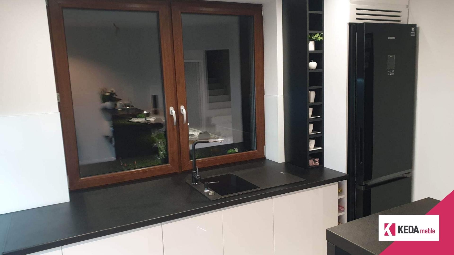 Kuchnia jest sercem domu, miejscem, gdzie rodzinne tradycje łączą się z nowoczesnym designem. W naszej ofercie znajdziesz rozwiązania, które harmonijnie łączą elegancję z funkcjonalnością, tworząc przestrzeń idealną dla każdej rodziny. Szczególnie polecamy biało-czarne kuchnie, które stanowią szczyt elegancji i są praktycznym wyborem dla każdego, kto ceni sobie styl i funkcjonalność w jednym. Elegancja w Kolorach: Biało-Czarne Kuchnie Kombinacja bieli i czerni w kuchni to ponadczasowy wybór, który nigdy nie wychodzi z mody. Białe powierzchnie odbijają światło, sprawiając, że kuchnia wydaje się większa i jaśniejsza. Czarne akcenty dodają z kolei głębi i charakteru, tworząc wyrafinowany kontrast. Duża Przestrzeń Robocza – Klucz do Funkcjonalności Przestronny blat roboczy to podstawa każdej dobrze zaprojektowanej kuchni. Pozwala na swobodną pracę i przygotowywanie posiłków bez zbędnego chaosu. W naszych projektach kładziemy duży nacisk na ergonomiczne rozmieszczenie elementów, aby każda czynność kuchenna była przyjemnością. Listwa LED – Rewolucja w Oświetleniu Kuchennym Odpowiednie oświetlenie to kluczowy element każdej kuchni. Nasze listwy LED nie tylko efektownie prezentują się w przestrzeni, ale także zapewniają doskonałe oświetlenie robocze, które jest niezbędne podczas przygotowywania posiłków. To praktyczne i energooszczędne rozwiązanie, które dodatkowo podkreśla nowoczesny charakter kuchni. Otwarte Półki – Praktyczne i Dekoracyjne Rozwiązanie Otwarte półki w słupku kuchennym to idealne miejsce na przechowywanie butelek wina, oliwy, czy ulubionych kubków do kawy. Dzięki temu Twoje ulubione przedmioty będą zawsze pod ręką, a jednocześnie staną się częścią dekoracji kuchni. Kuchnie na Wymiar – Twój Indywidualny Projekt Dołącz do grona zadowolonych klientów, zamawiając kuchnię na wymiar. Nasze projekty są w pełni dostosowane do potrzeb i oczekiwań każdego klienta. Tworzymy kuchnie, które są nie tylko piękne, ale przede wszystkim praktyczne i funkcjonalne. Podsumowanie Nasze biało-czarne kuchnie to idealne połączenie elegancji i funkcjonalności. Jeśli marzysz o kuchni, która będzie nie tylko piękna, ale także praktyczna i wygodna, zapraszamy do kontaktu. Zrealizujemy dla Ciebie projekt, który spełni wszystkie Twoje oczekiwania.